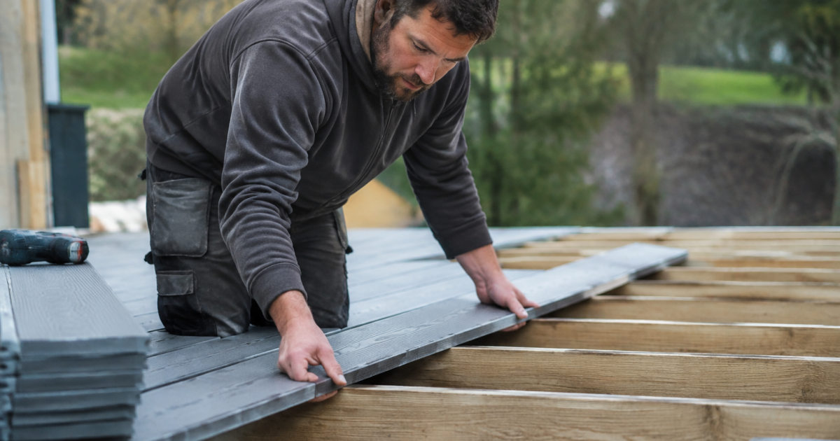 Ouvrier aligne planches grises sur structure bois