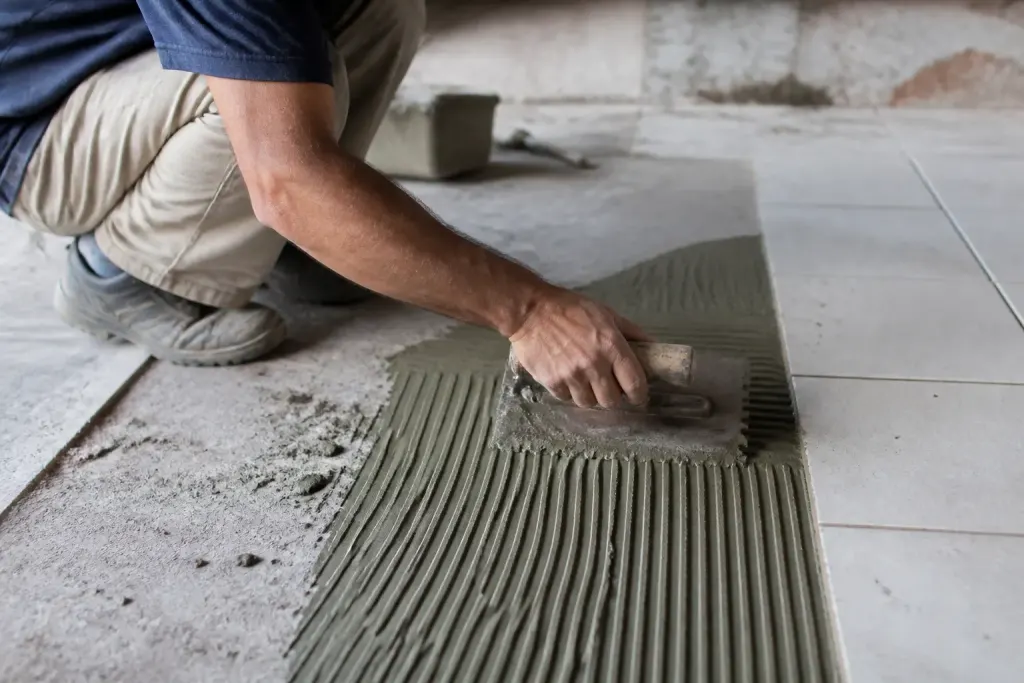 Ouvrier etale colle avec spatule crantee sur carreau emaille