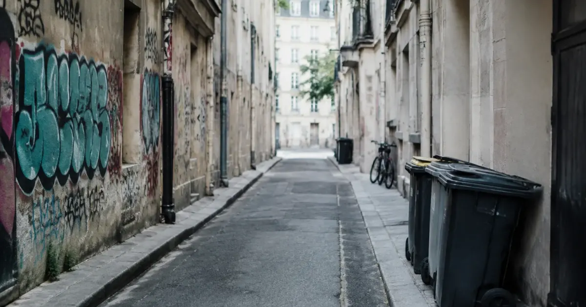 Ruelle déserte, murs tagués, poubelles posées contre le trottoir